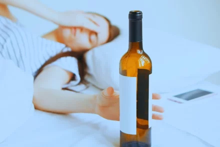 Drunk women lying on her bed reaching a bottle of wine.